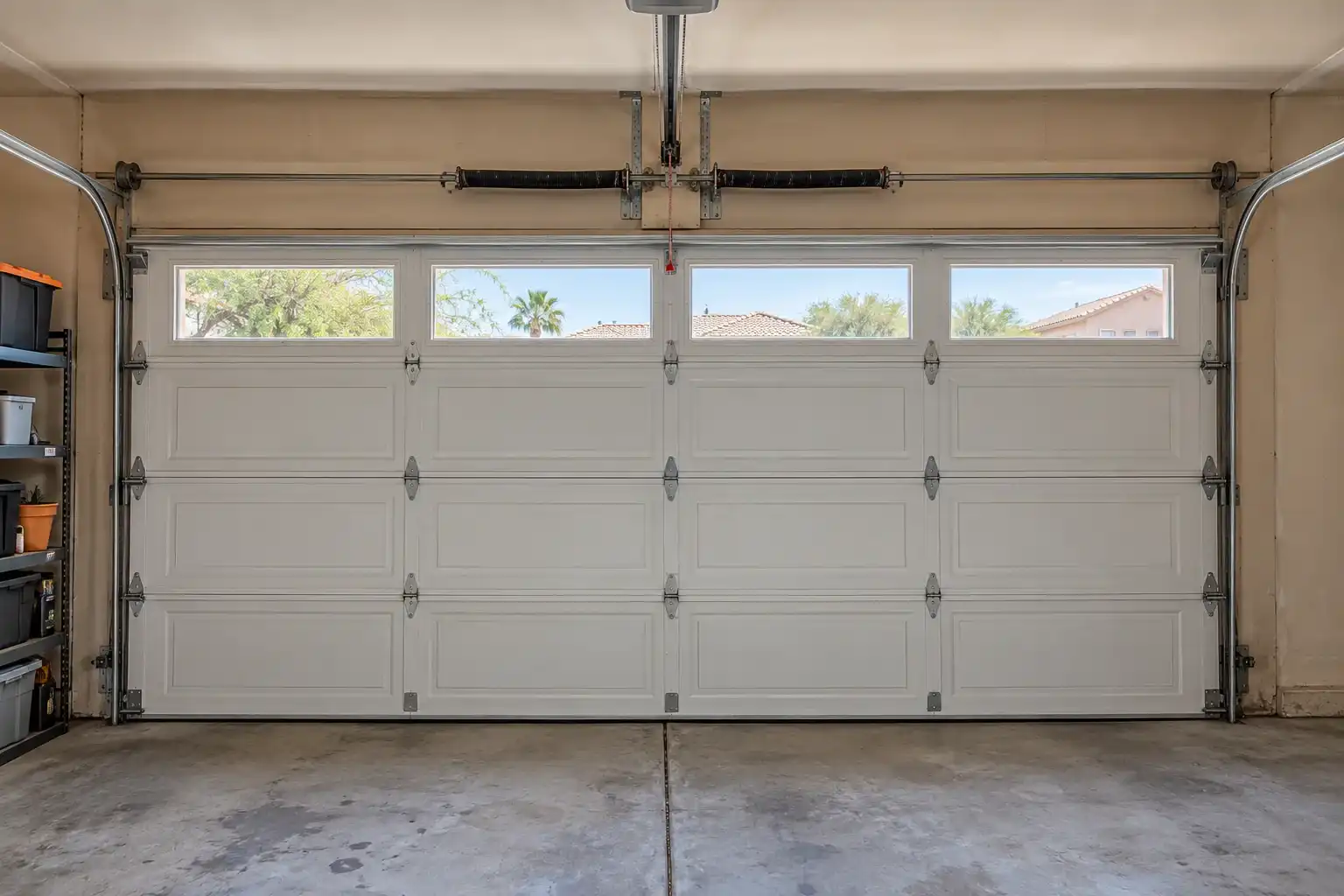 Inside a garage: a closed white door with windows, torsion springs, side tracks and the opener rail