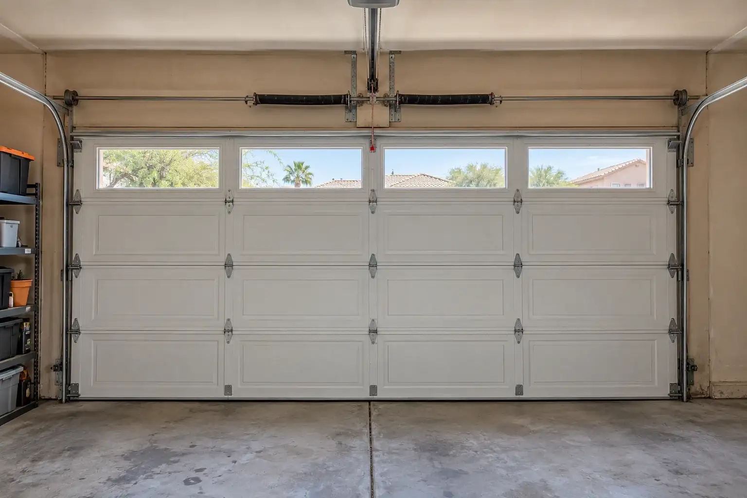 Inside a garage: a closed white door with windows, torsion springs, side tracks and the opener rail